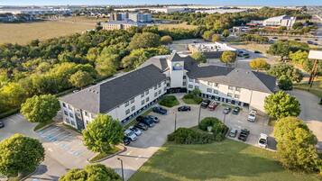 An aerial view of a hotel with multiple parking spaces, a central courtyard, and surrounding greenery.
