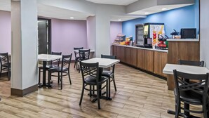 A restaurant with multiple tables and chairs, a counter with kitchen appliances, and a wooden floor. - Days Inn & Suites by Wyndham DeSoto (DeSoto)