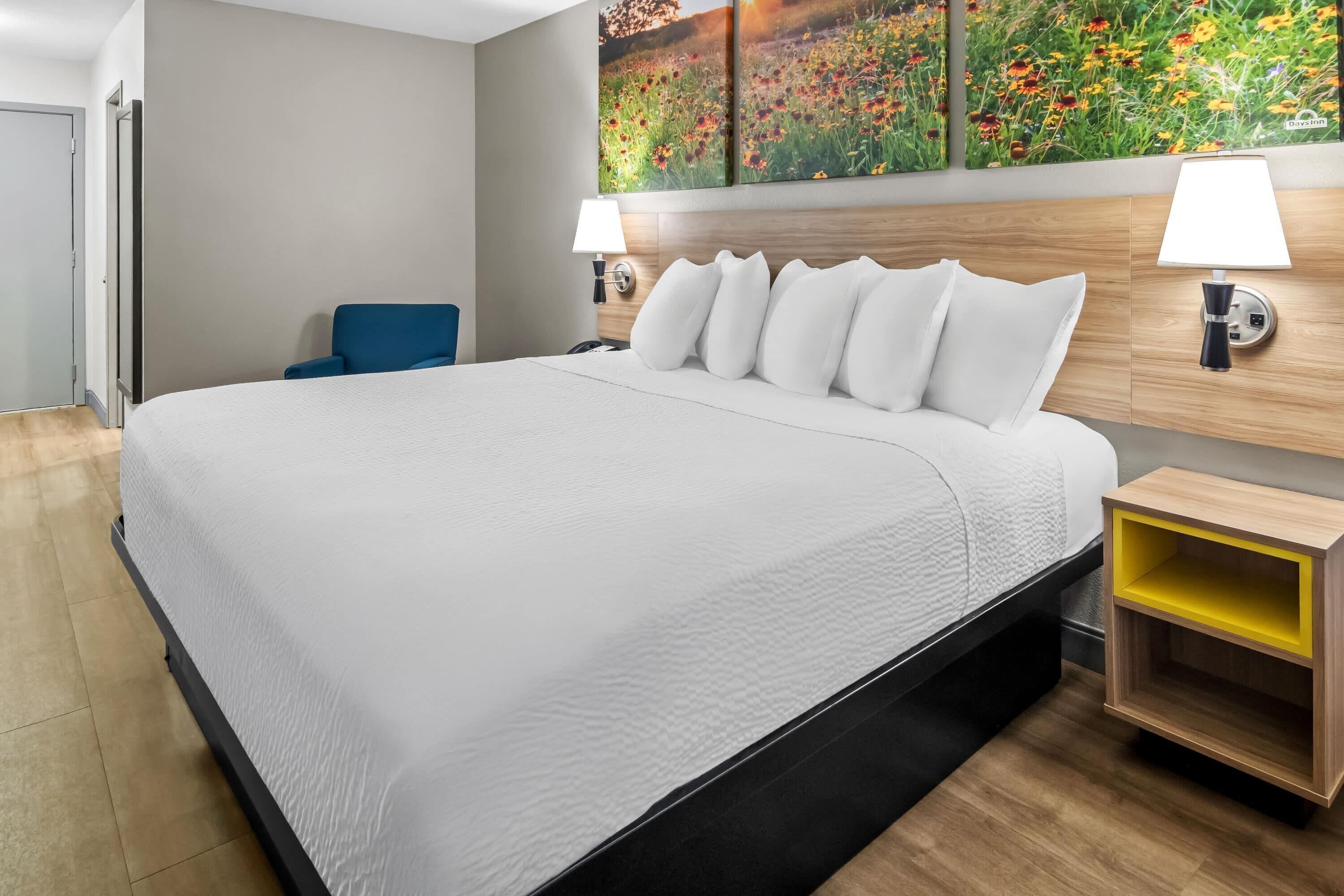 A hotel room with a large bed, two bedside lamps, a wooden headboard, and a wall-mounted shelf.