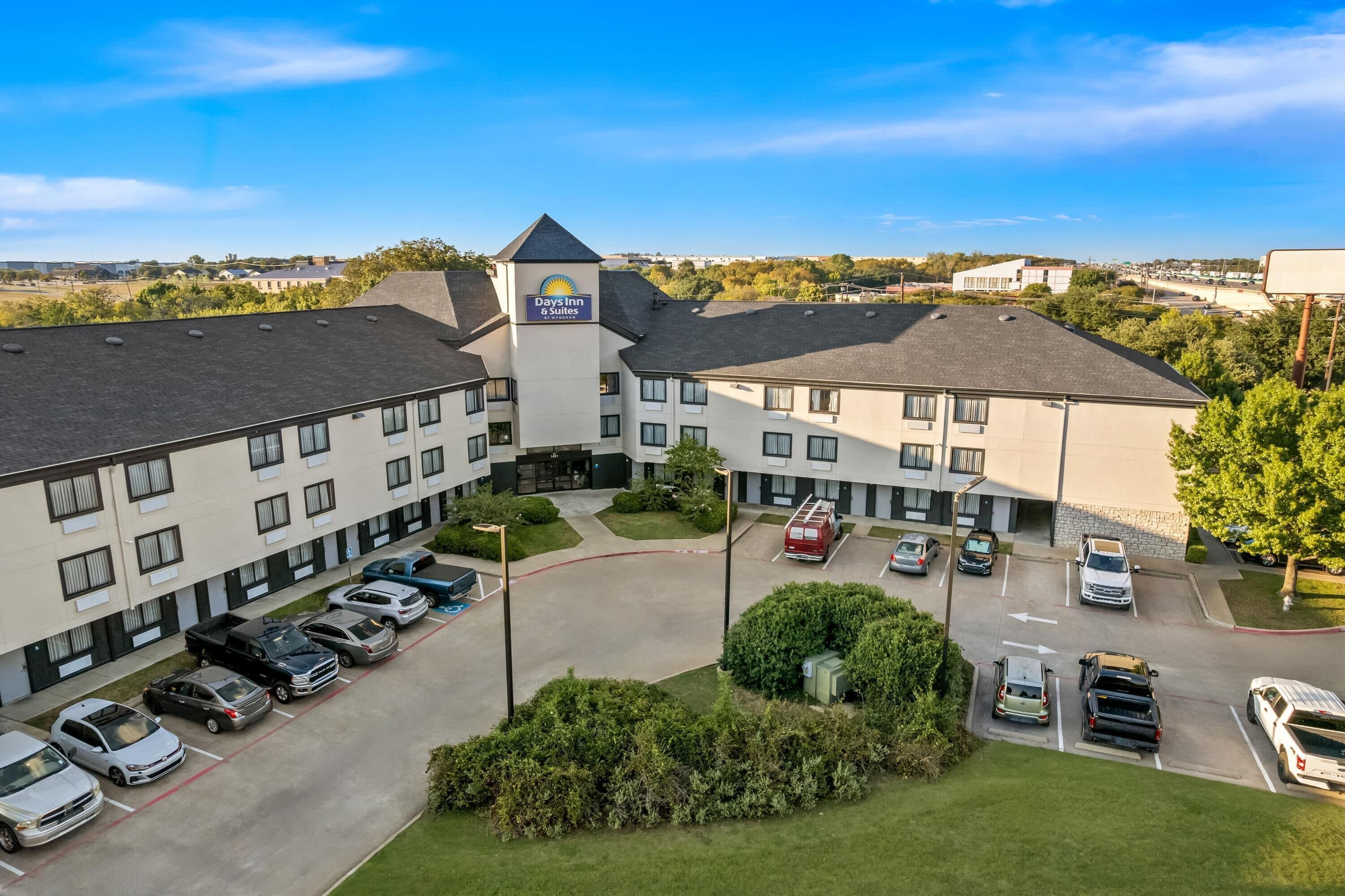 Un hotel Days Inn & Suites con estacionamiento, varias edificaciones y cielo despejado.