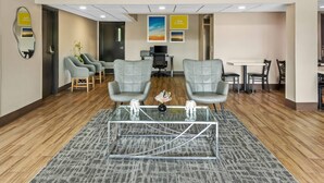 A lobby with a reception desk, two grey armchairs, a glass coffee table, and a patterned rug. - Days Inn & Suites by Wyndham DeSoto (DeSoto)