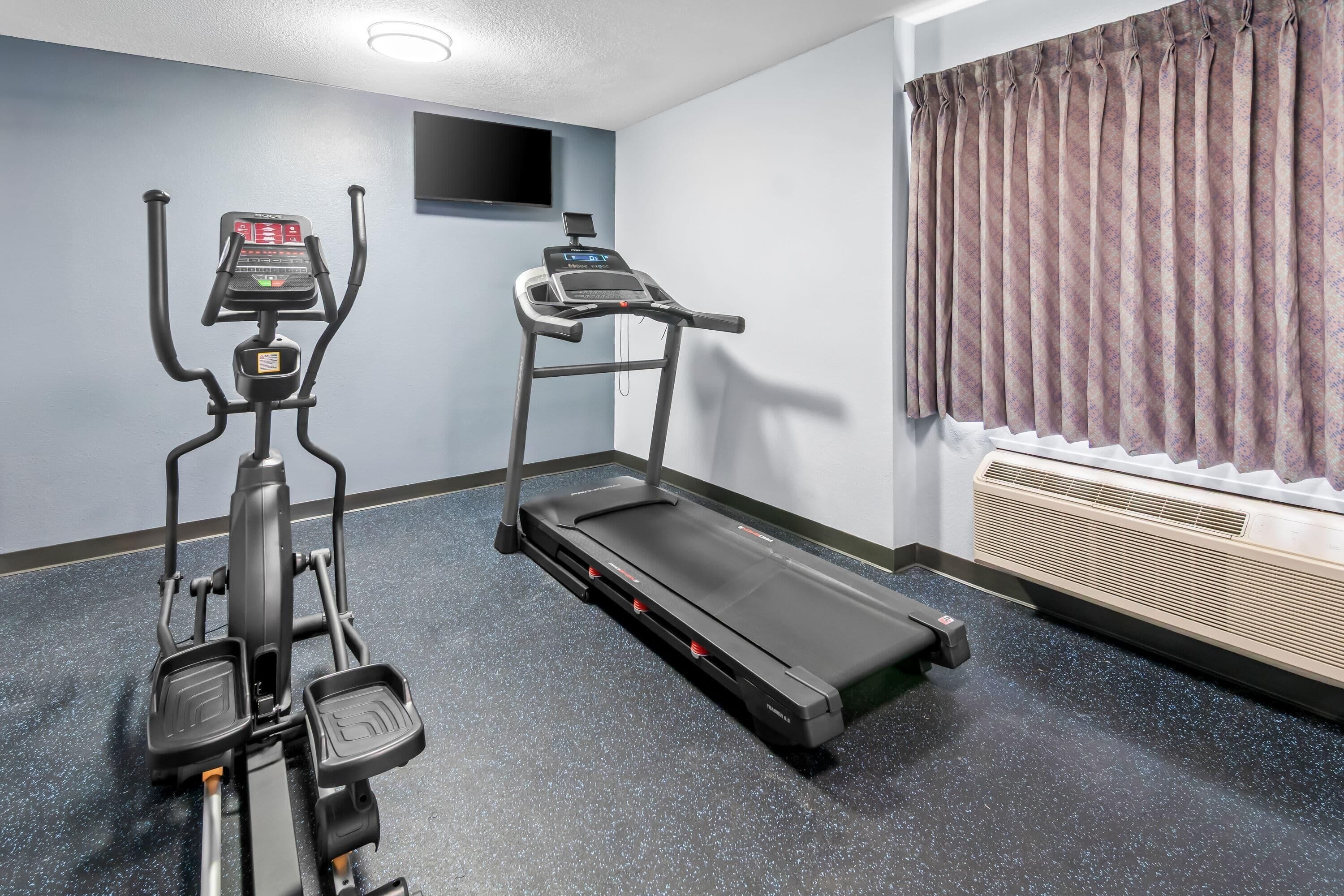 A fitness room with an elliptical, a treadmill, and a wall-mounted TV.