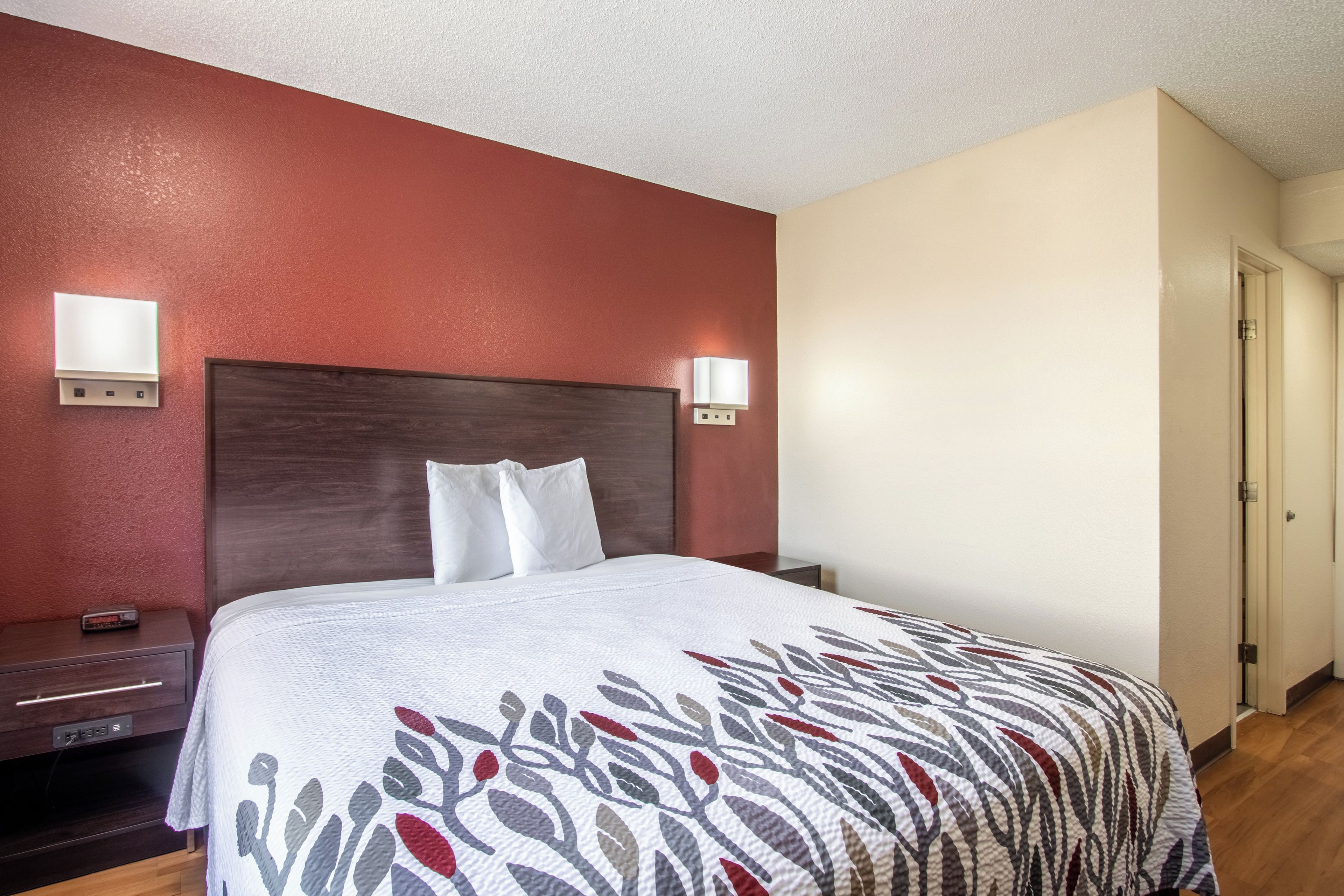 A hotel room with a bed, bedside tables, and wall-mounted lights.