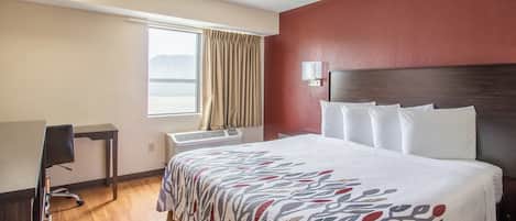 Habitación de hotel con cama, escritorio, ventana con cortinas, lámpara de pared y calefactor.