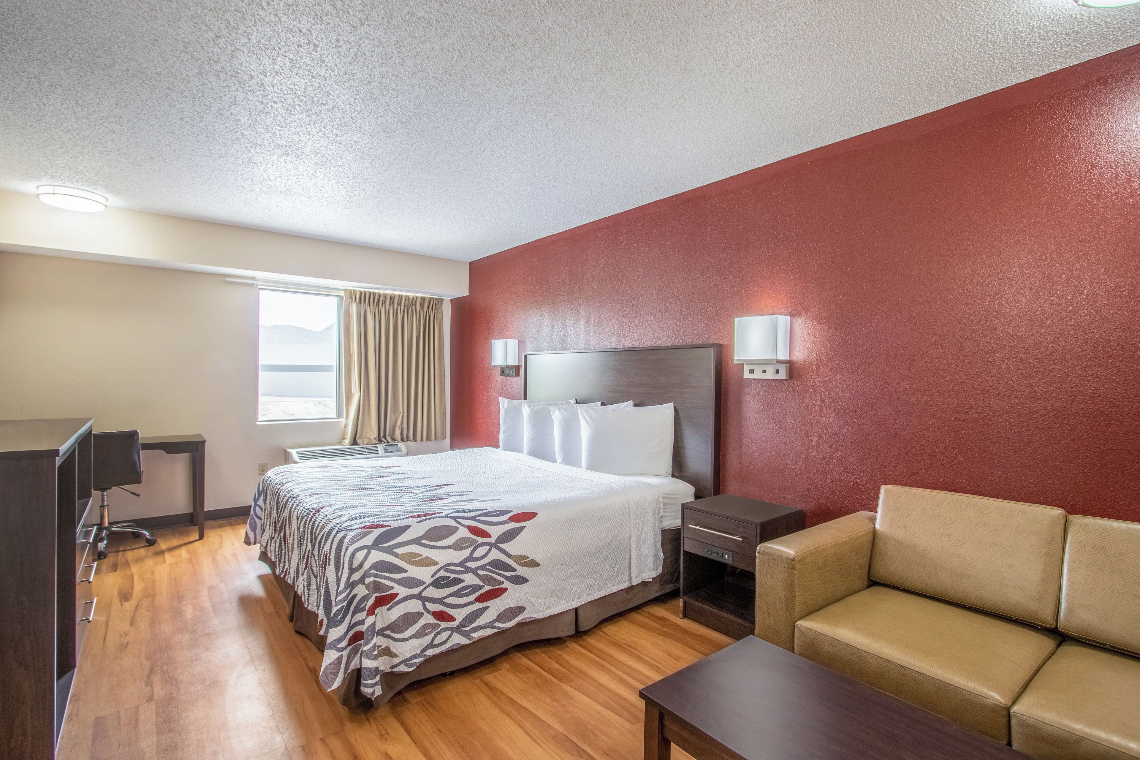 Ein Hotelzimmer mit Bett, Schreibtisch, Stuhl, Sofa und Fernseher.