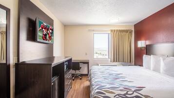 A hotel room with a bed, a desk, a chair, a television, a window with curtains, and a view of the outside.