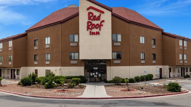 Un hotel Red Roof Inn con fachada marrón, múltiples ventanas y techo rojo.