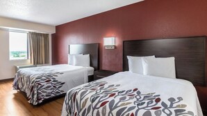 Habitación de hotel con dos camas, un ventanal con cortinas y una pared roja.