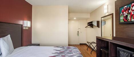 A hotel room with a bed, a TV, a desk, and a mirror.