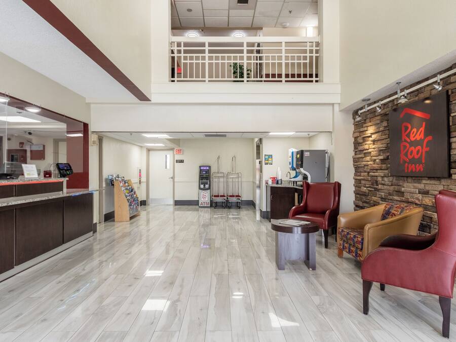 Una hall d'albergo con una reception, bancomat, un'area salotto con poltrone, una scala e il cartello Red Roof Inn.