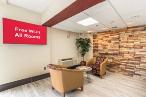A waiting area with a sign indicating free Wi-Fi availability, a potted plant, two leather chairs, a small table, and a stone wall. - Red Roof Inn El Paso West (El Paso)