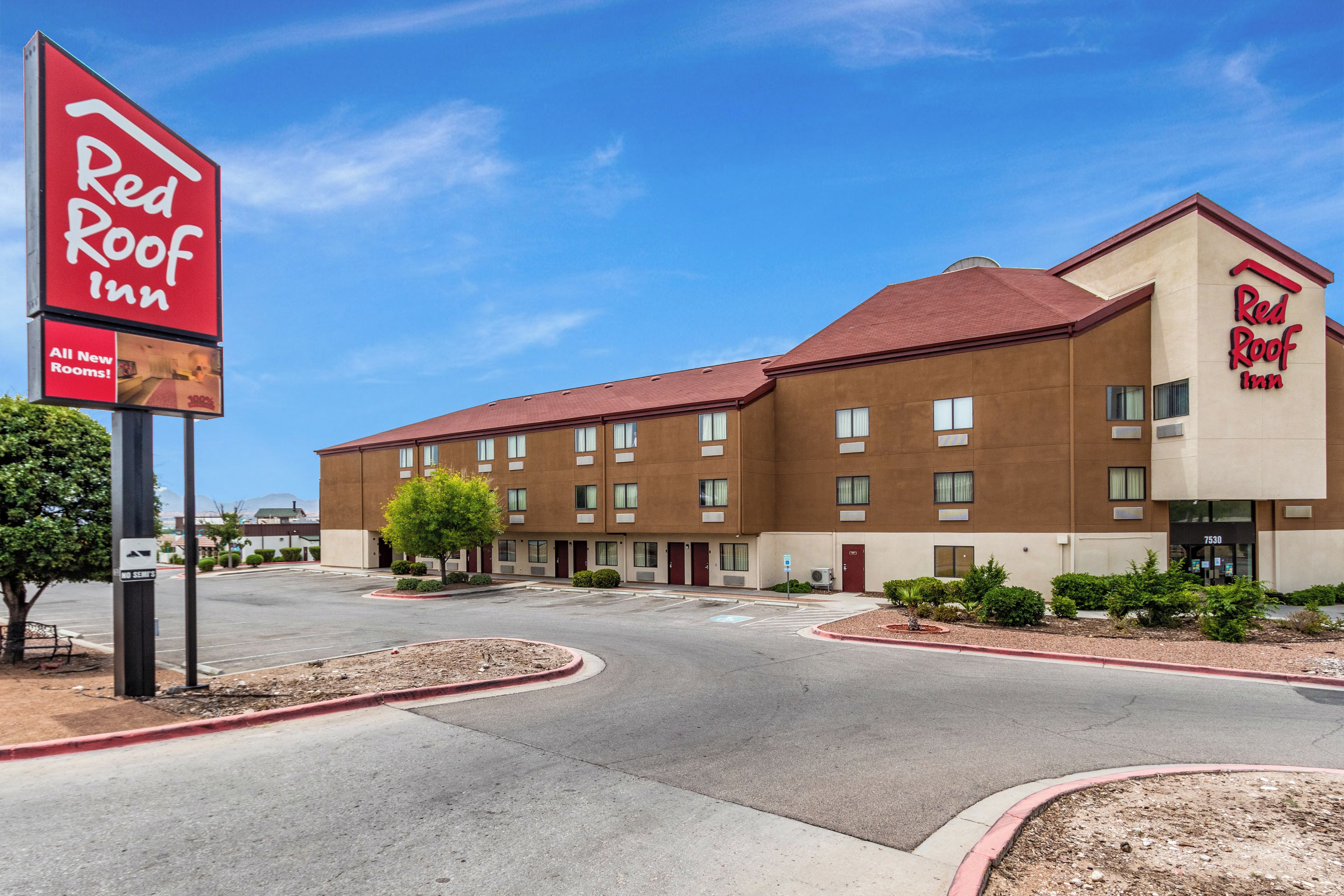 Un hôtel Red Roof Inn avec un ciel dégagé, un parking et un bâtiment doté de nombreuses fenêtres et portes.