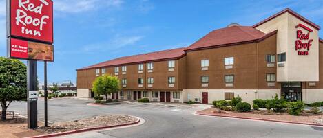 A Red Roof Inn with a clear sky, a parking lot, and a building with multiple windows and doors.