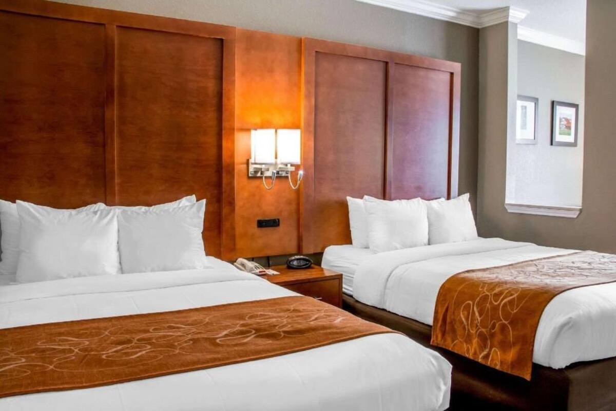 A hotel room with two beds, a wooden headboard, a nightstand with a phone, and a wall-mounted light.