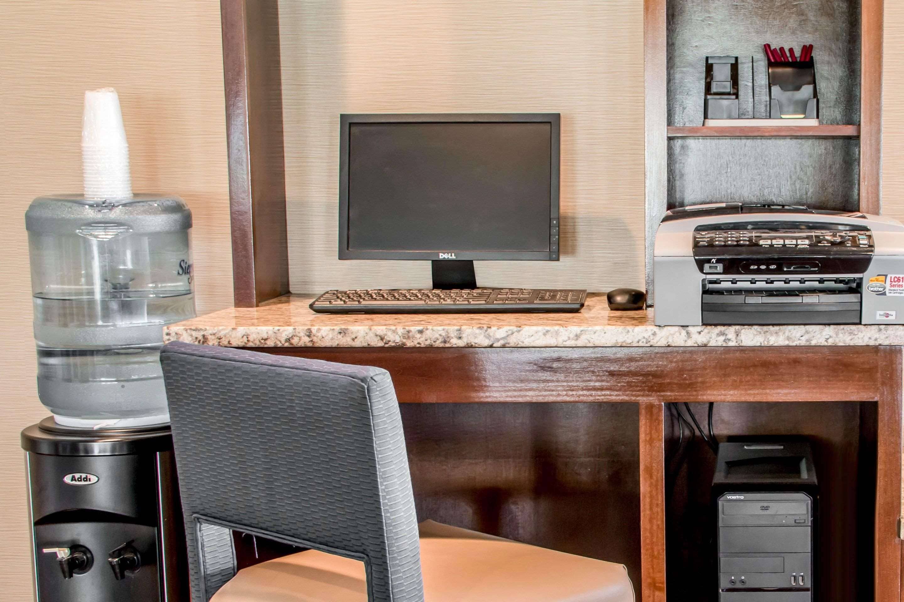 Une chambre d’hôtel équipée d’un bureau, d’un écran d’ordinateur, d’un clavier, d’un distributeur d’eau, d’une chaise et d’une imprimante.