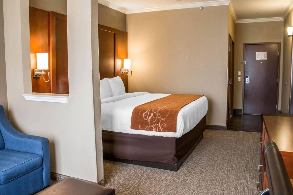 A hotel room with a bed, a desk, a chair, and a door.