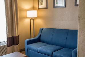 A blue sofa, a floor lamp, and a small table in a hotel room.