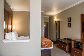 A hotel room with a bed, a desk with a microwave, a dresser, a mirror, and a door leading to another room.