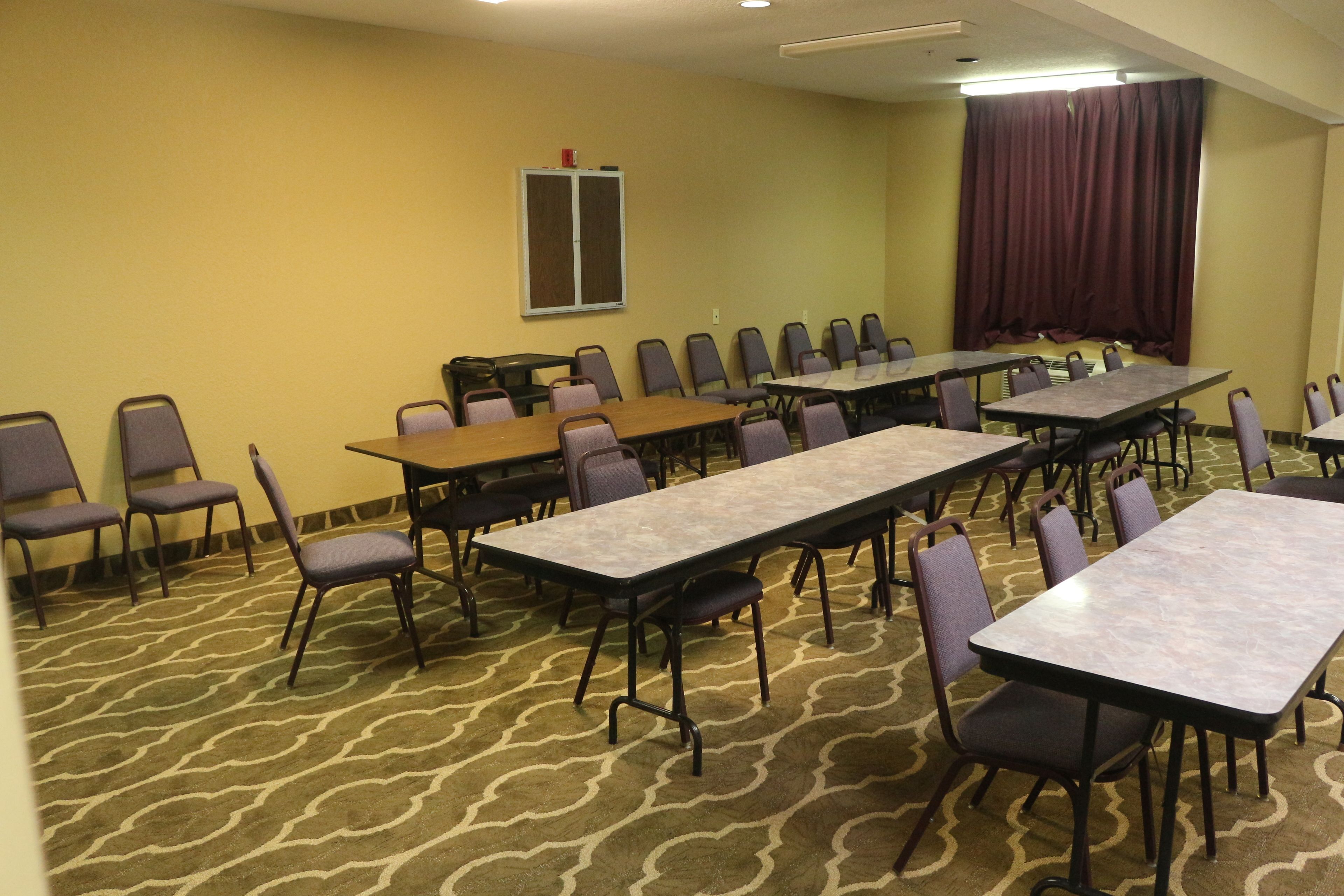 A conference room with multiple tables and chairs, carpeted floor, and a large window with curtains.
