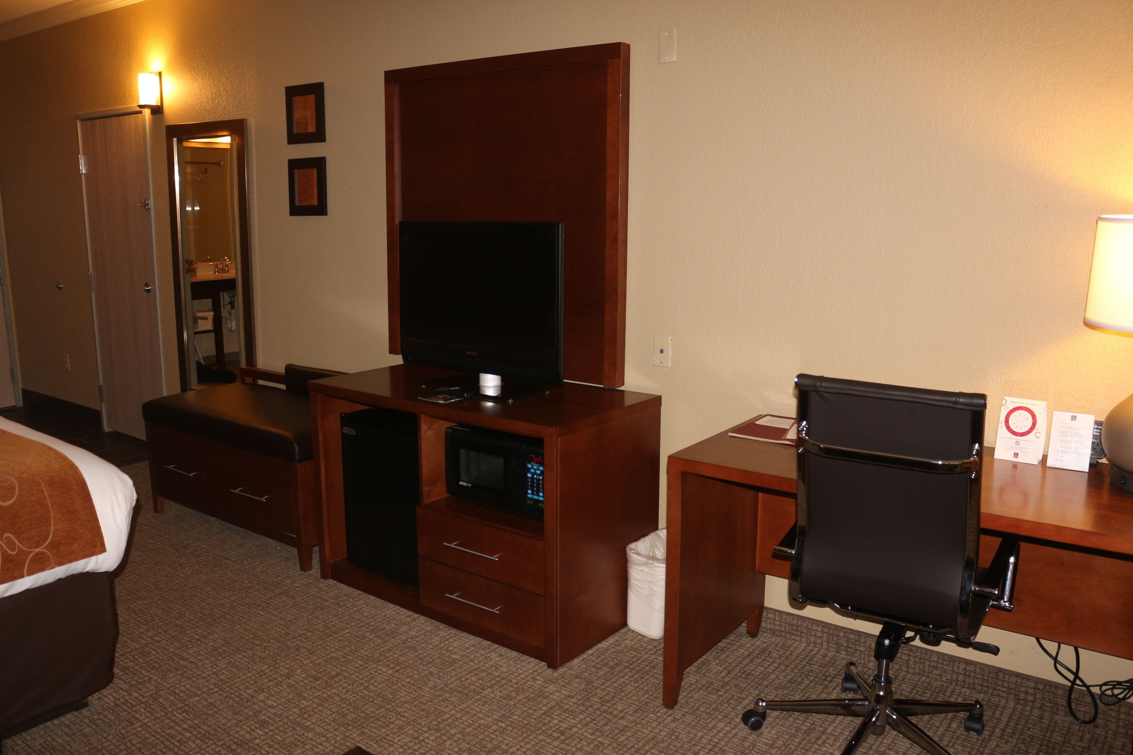 Habitación de hotel con una cama, un escritorio con computadora, televisión, microondas, bote de basura y lámpara.
