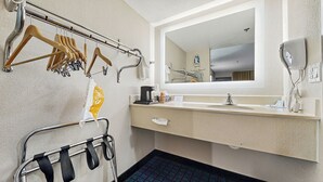 A hotel bathroom with a sink, mirror, towel rack, and a shower area.