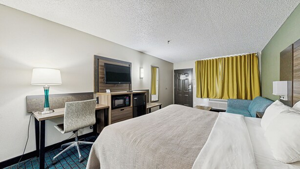 A hotel room with a bed, desk, chair, television, and a small refrigerator.
