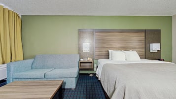 A hotel room with a bed, a sofa, a small table, and a nightstand with a lamp.