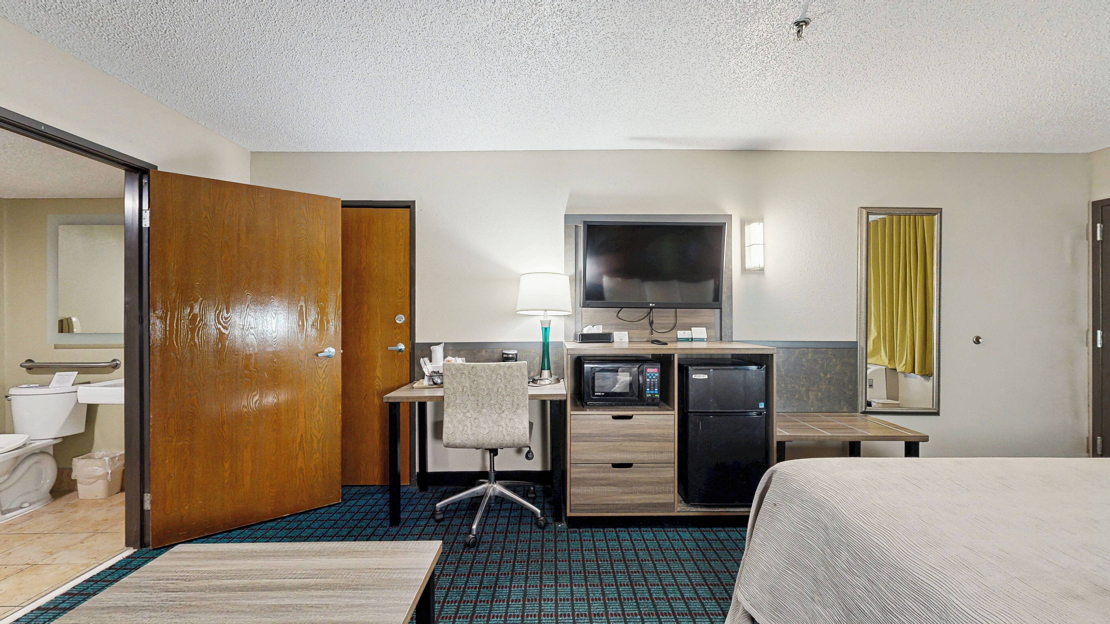A hotel room with a bed, desk, chair, television, and a small refrigerator.