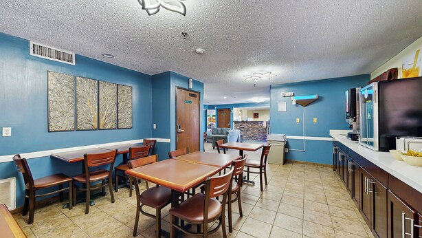 A restaurant with blue walls, wooden tables and chairs, and a kitchen area with a refrigerator and coffee machine. - Quality Inn Van Horn (Van Horn)
