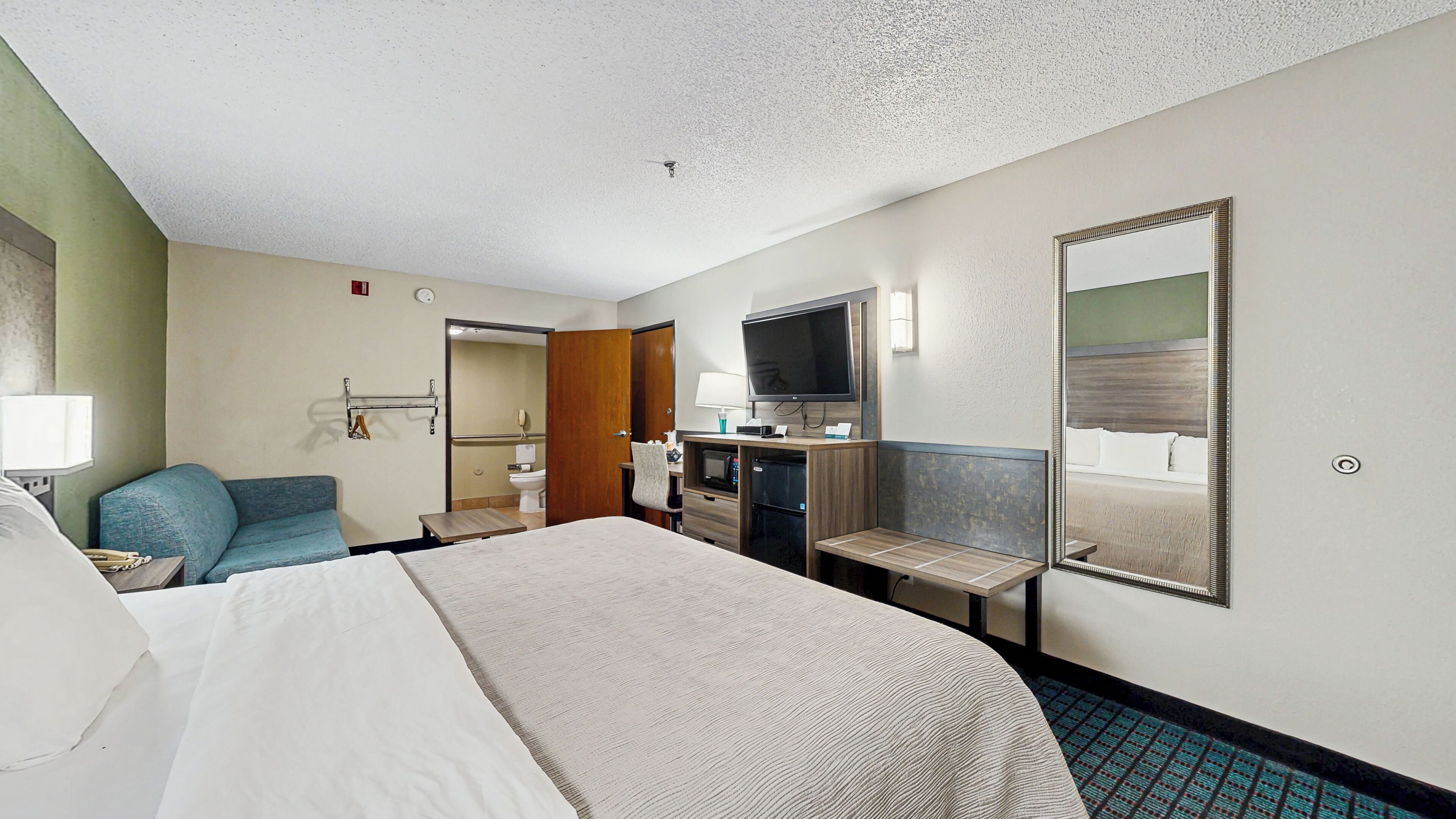 Una habitación de hotel con cama, escritorio, silla, televisor y espejo.