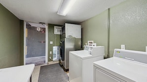 A compact hotel room with a kitchenette, a washing machine, and a small shower area.