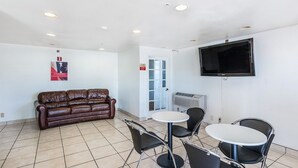 Una habitación con un sofá de cuero marrón, un televisor montado en la pared y una mesa pequeña con cuatro sillas.