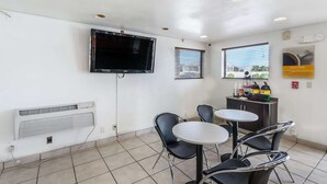 Una habitación pequeña y limpia con una televisión de pantalla plana, dos ventanas con persianas, una mesa con cuatro sillas y una zona de kitchenette con estufa y refrigerador.