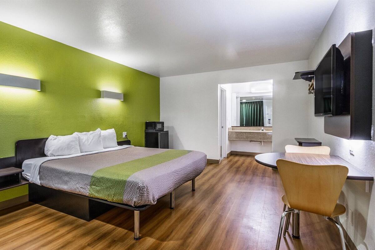 A hotel room with a bed, bedside table, chair, and a small desk with a chair.