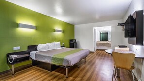 A hotel room with a bed, bedside table, chair, and a small desk with a chair. - Motel 6 San Marcos, TX - North (San Marcos)