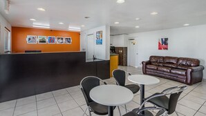 Un área de recepción con mostrador, un sofá de cuero marrón y dos mesas redondas con sillas.