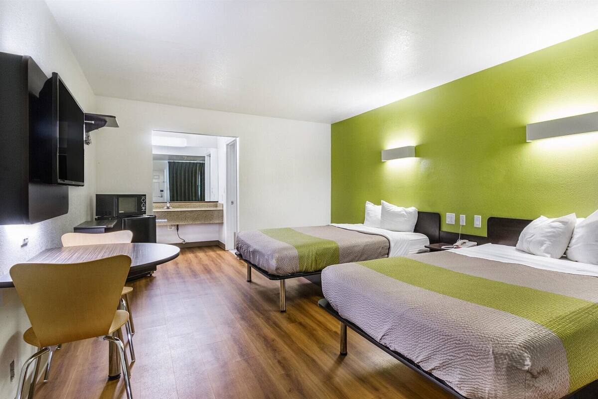 A hotel room with two beds, a desk, and a TV.