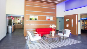 A lobby with a red sofa, white armchairs, a coffee table, and a vending machine.