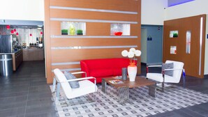 A modern lobby with a red sofa, white armchairs, a wooden partition with glass panels, and a patterned floor.