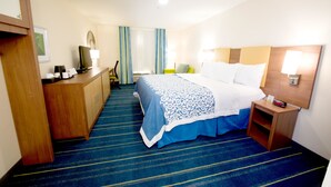 A hotel room with a bed, bedside table, lamp, and a desk with a chair.