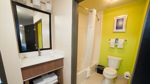 A bathroom with a white sink, mirror, and toilet, a shower with a curtain, and a green wall.