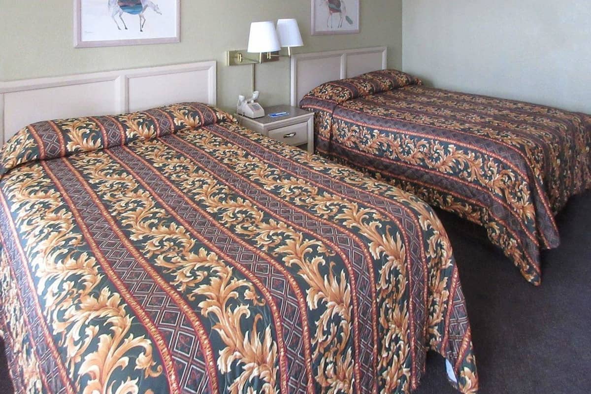 A hotel room with two beds, a nightstand, a lamp, and two framed pictures on the wall.