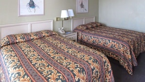 A hotel room with two beds, each with patterned bedspreads, a nightstand with a lamp, and two framed pictures on the wall. - Rodeway Inn San Juan (San Juan)
