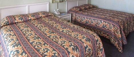 Habitación de hotel con dos camas, cada una con colchas estampadas, una mesita de noche con lámpara y dos cuadros enmarcados en la pared.