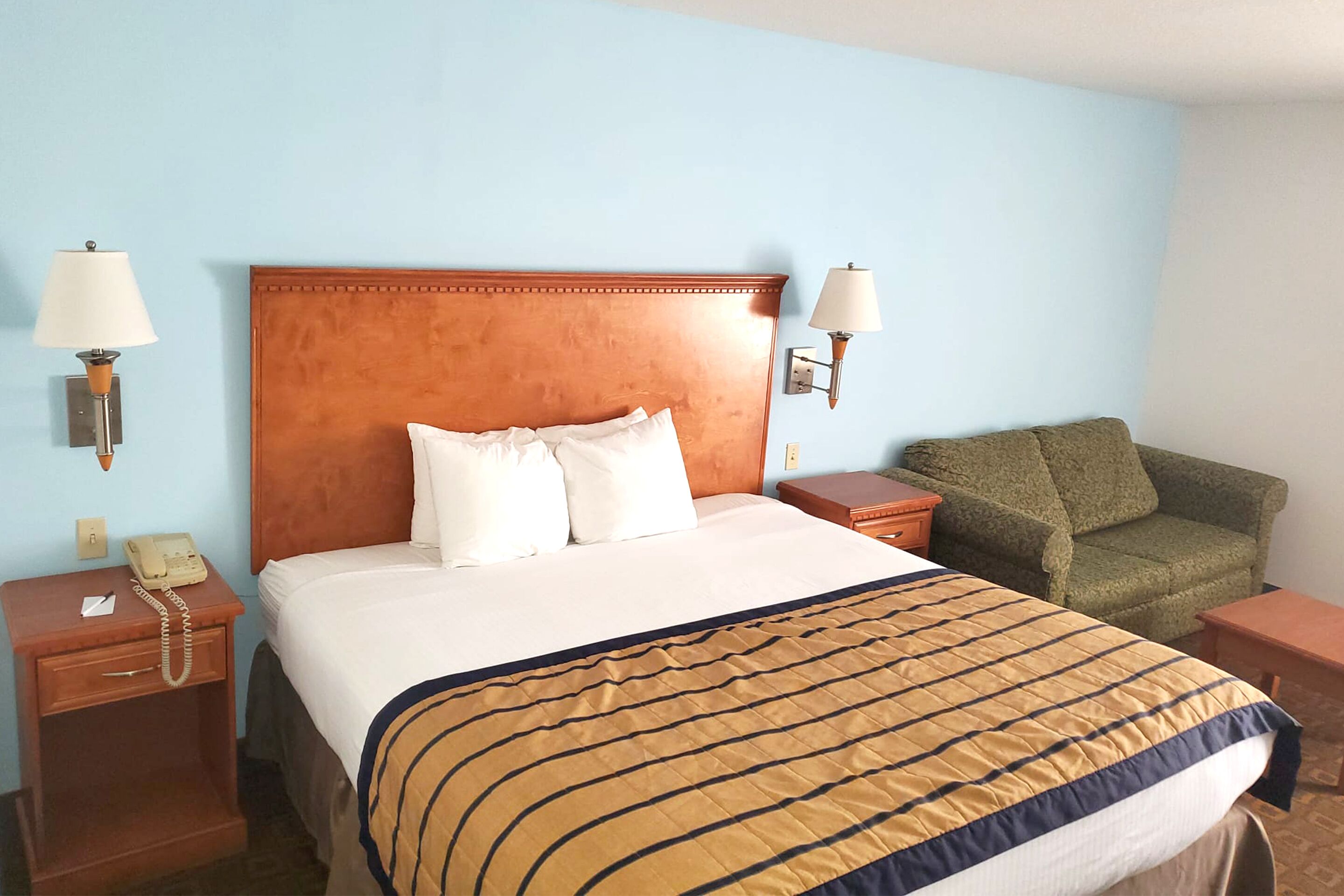 Habitación de hotel con una cama grande, dos mesitas de noche, un sillón verde y un buró con teléfono.
