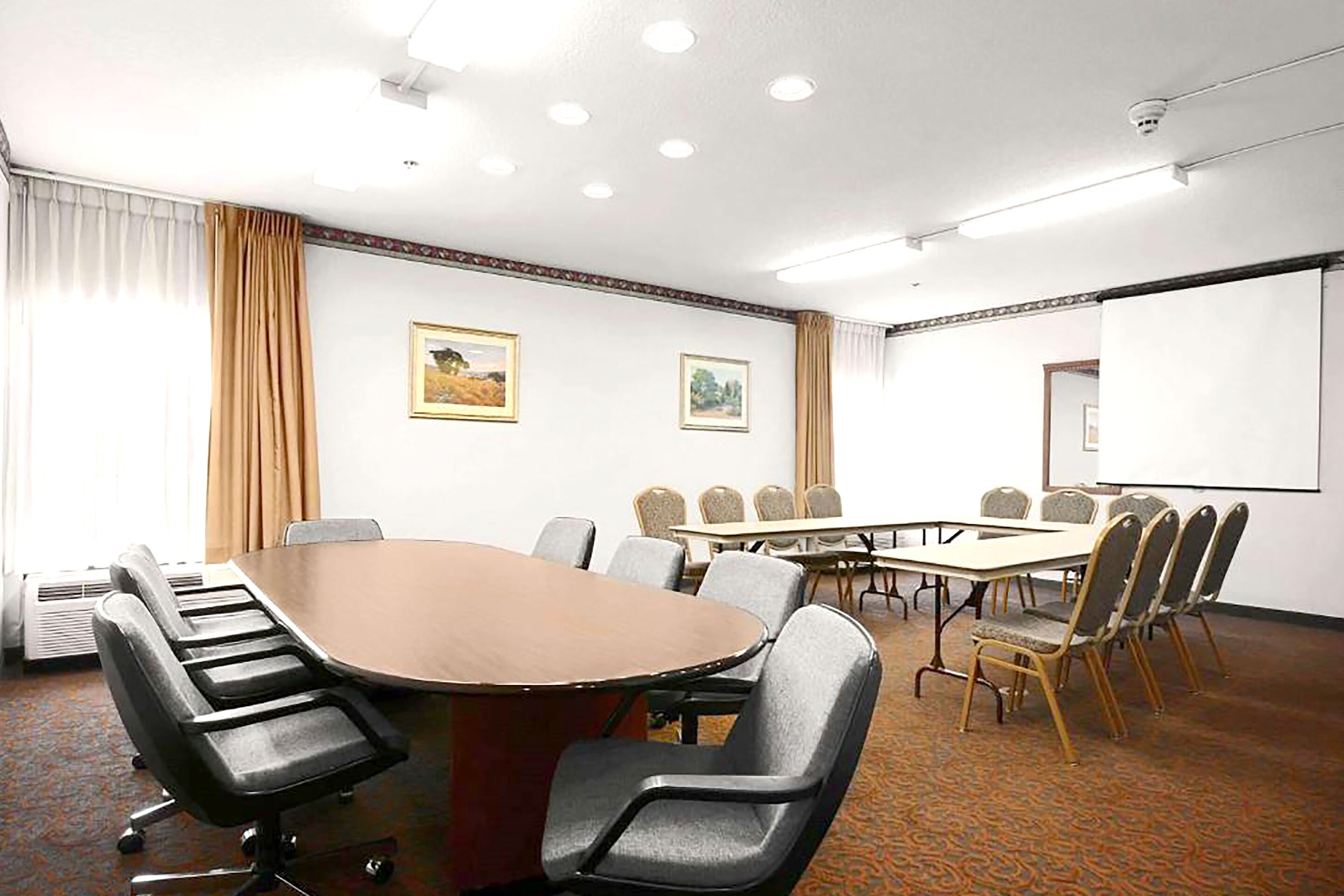 Een vergaderzaal met een grote ovale tafel, meerdere stoelen en een projectiescherm.
