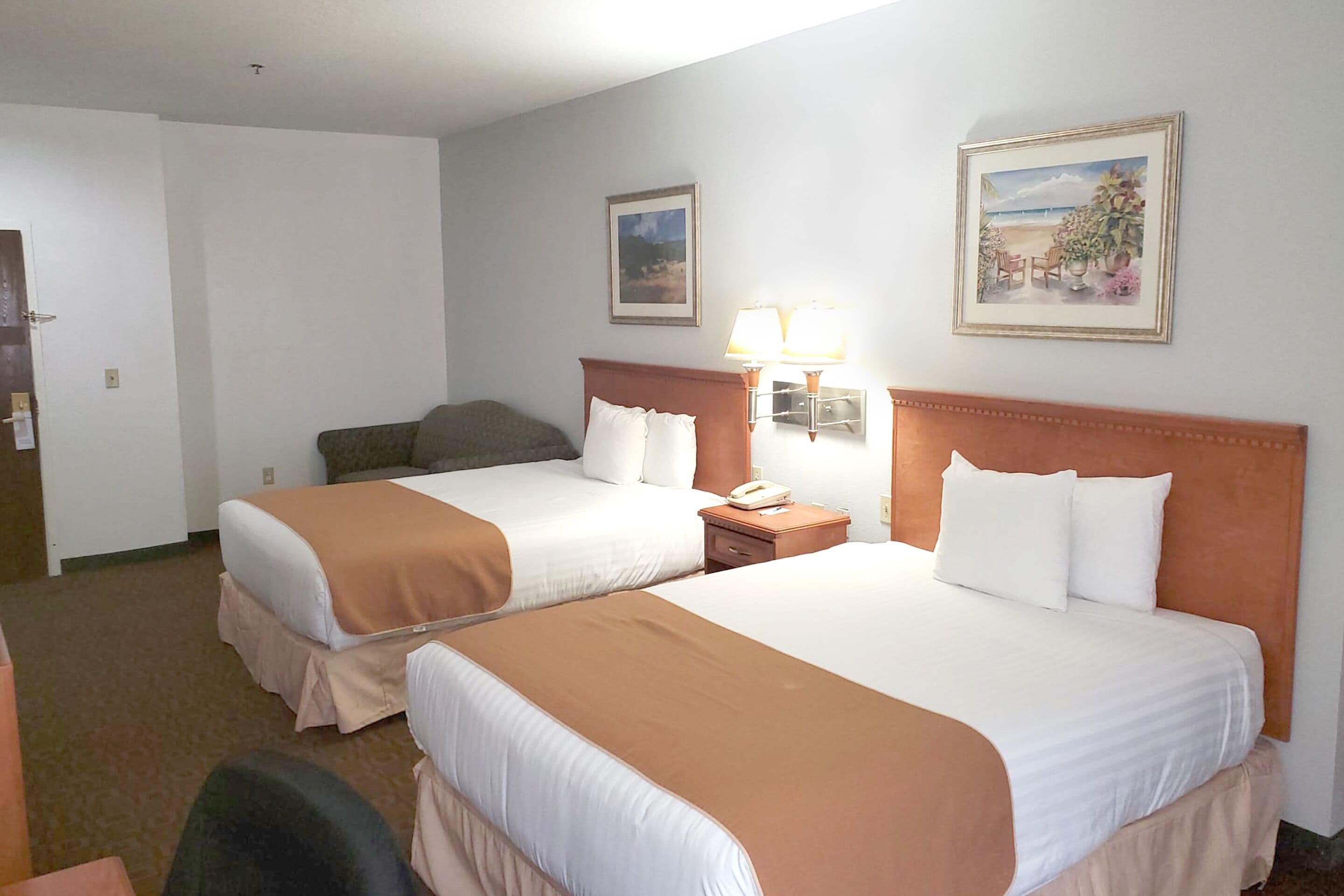 Een hotelkamer met twee bedden, een nachtkastje met een lamp en twee ingelijste foto's aan de muur.