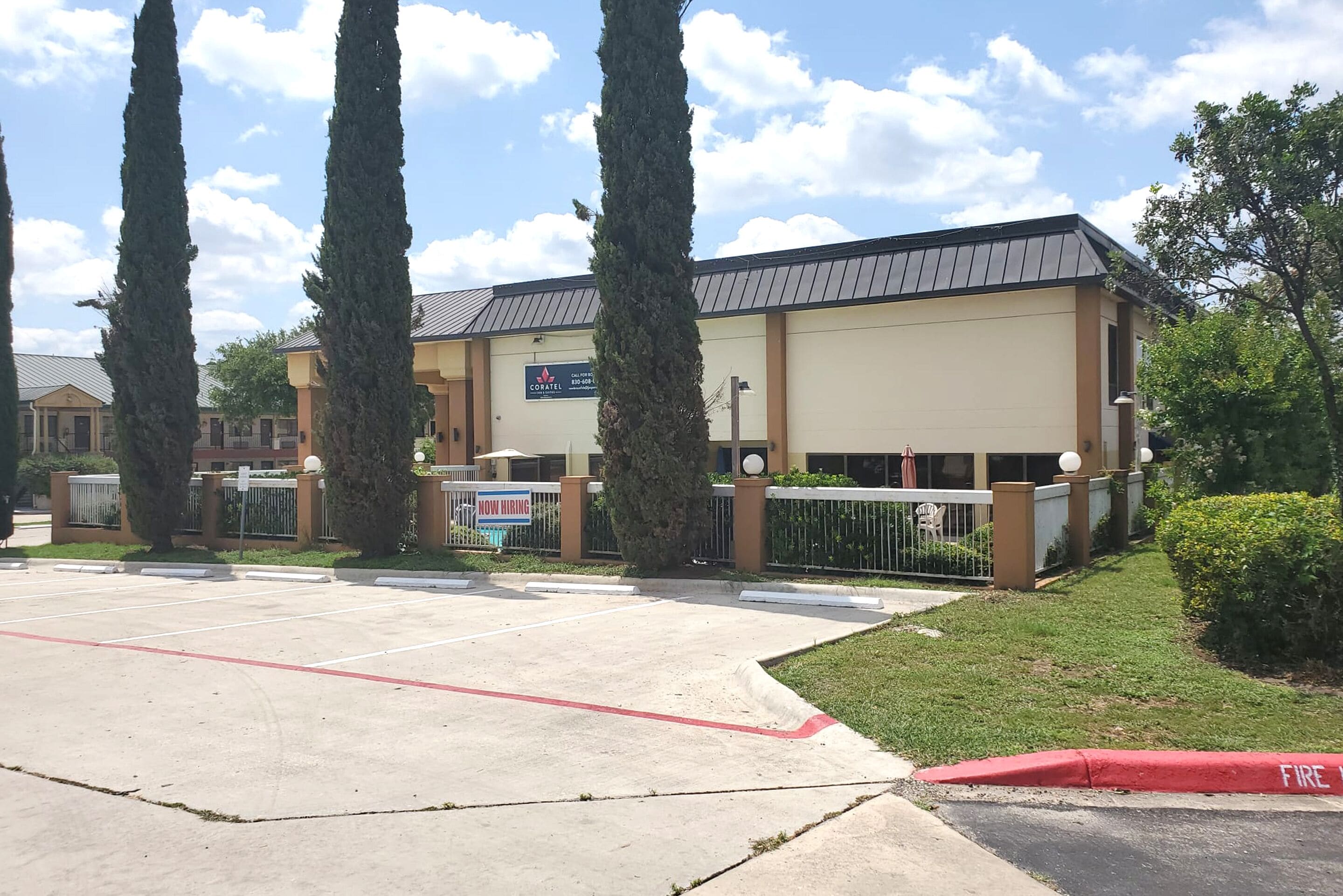 Un edificio con un letrero que dice 'CORATE' y un aviso de 'Se busca personal', rodeado de árboles y un estacionamiento.