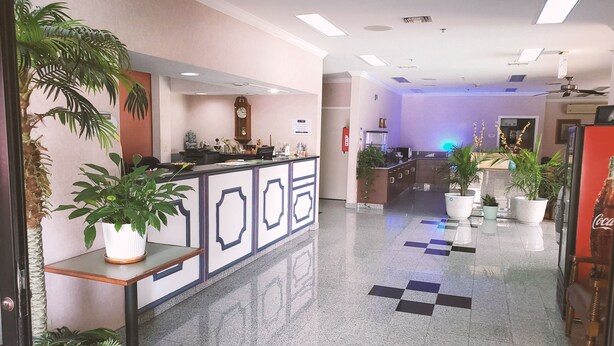 A hotel lobby with a reception desk, potted plants, a clock, and a check-in counter. - Coratel Inn & Suites by Jasper New Braunfels IH-35 EXT 189 (New Braunfels)