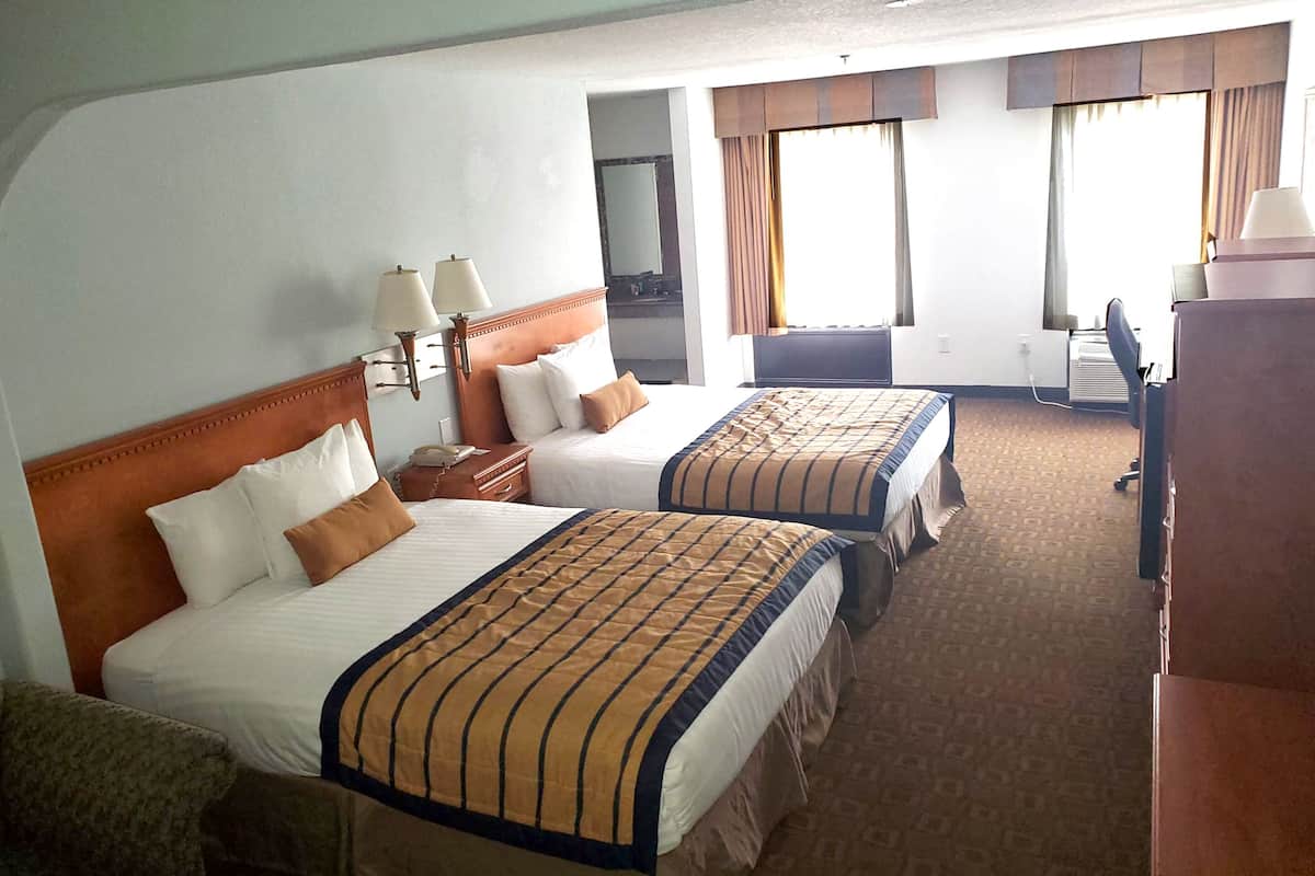 A hotel room with two beds, a desk, a chair, and a wardrobe.